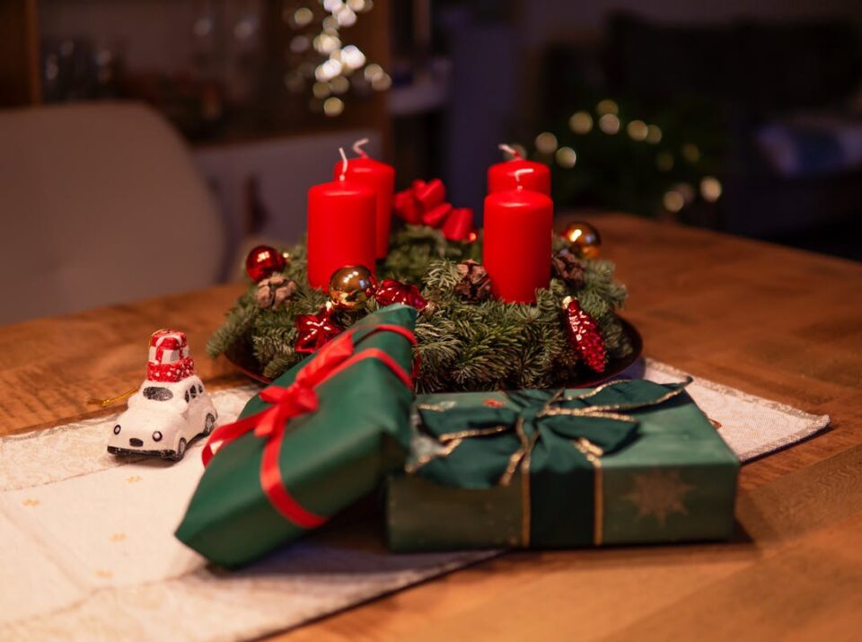 Cozy Christmas scene featuring red candles, gifts, and decorations on a wooden table.