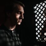 A priest listens to a penitent in a dimly lit confessional, embodying themes of faith and repentance.