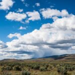 Vast landscape featuring fluffy clouds over a serene grassland and distant hills.