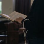 Person holding a holy book with prayer beads inside a church. Spiritual and religious setting.