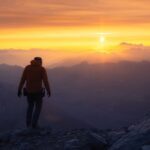 A lone hiker silhouetted against a vibrant mountain sunrise.