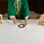 A priest in green vestments prepares the sacramental bread during a Catholic mass ceremony.
