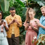 Four adults using smartphones surrounded by lush greenery in an outdoor setting, enjoying technology in nature.