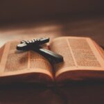 Close-up of an open Bible with a wooden cross inscribed with 'Hope' on a table.
