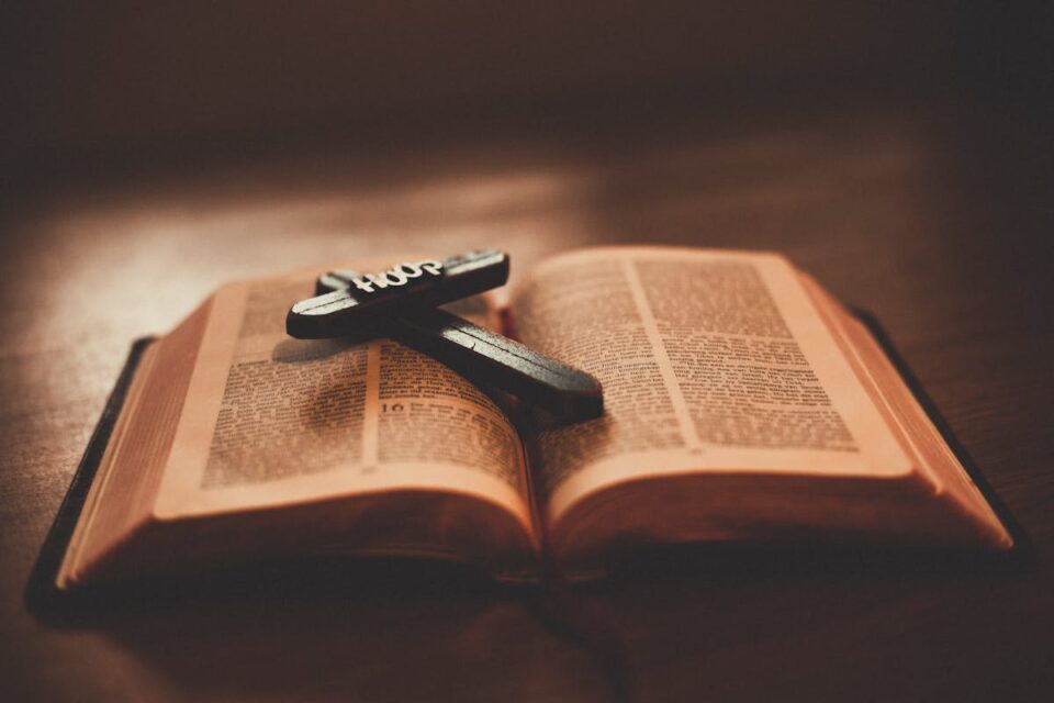 Close-up of an open Bible with a wooden cross inscribed with 'Hope' on a table.