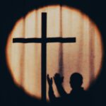 a silhouette of a person holding a cross in front of a window
