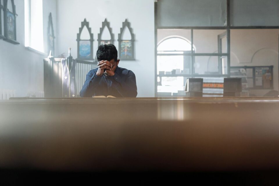 A man in prayer in a sunlit room, reflecting spirituality and peace.