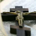 An open Bible with a brass crucifix on a dark wooden cross lying across it.