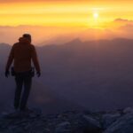 A lone hiker silhouetted against a vibrant mountain sunrise.