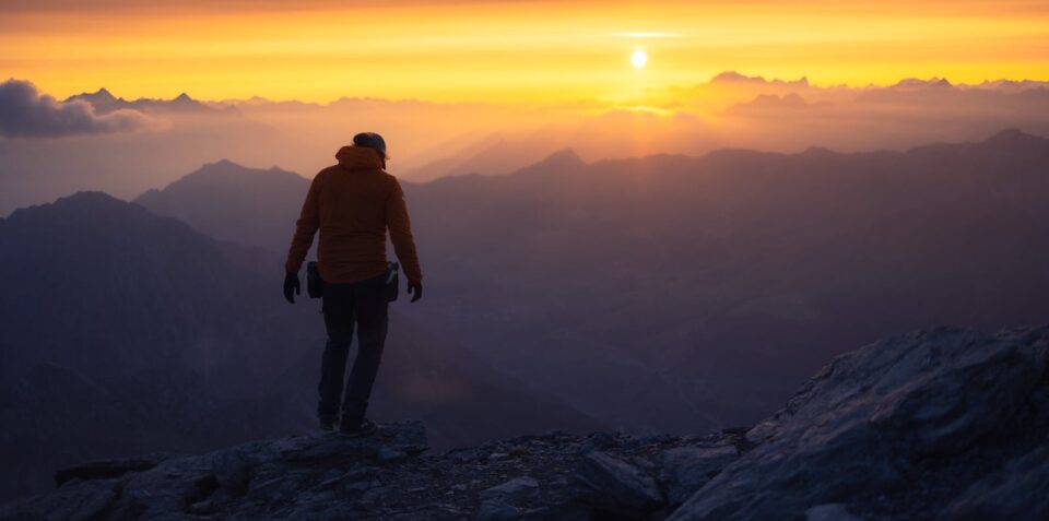 A lone hiker silhouetted against a vibrant mountain sunrise.