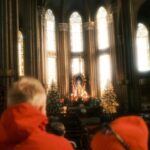 Visitors in a cathedral admire the altar adorned with Christmas decorations and sunlight.