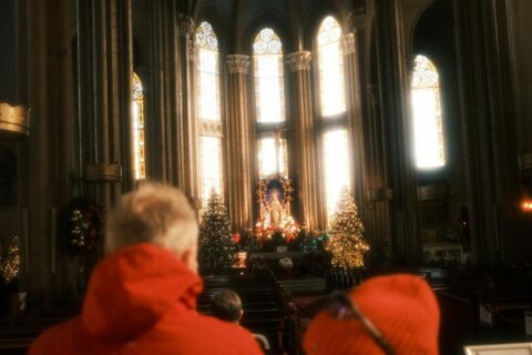 Visitors in a cathedral admire the altar adorned with Christmas decorations and sunlight.
