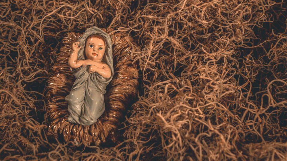 A nativity scene featuring a baby Jesus figurine surrounded by straw, symbolizing hope and tradition.