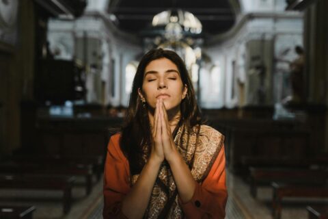A woman with closed eyes prays in a peaceful cathedral setting, conveying a sense of calm and spirituality.
