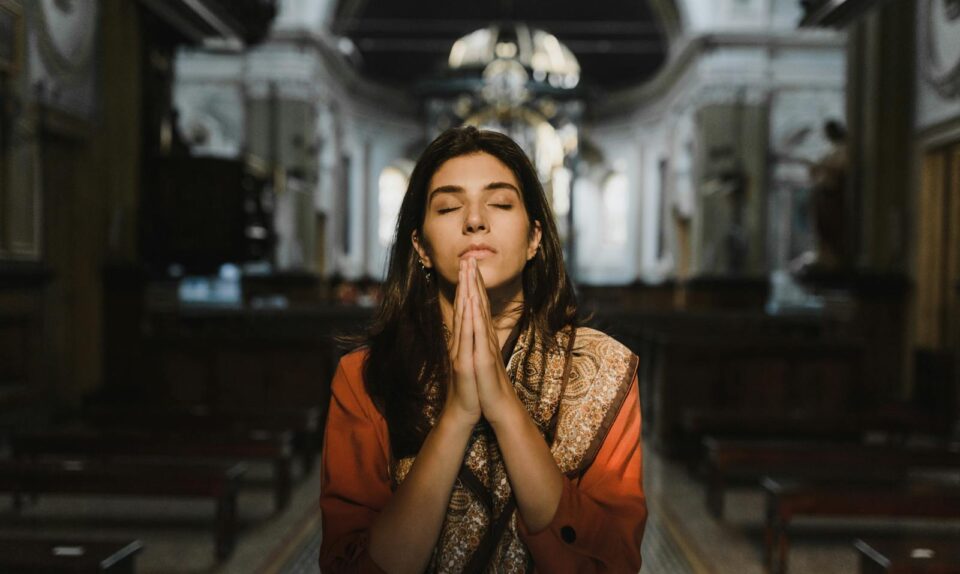 A woman with closed eyes prays in a peaceful cathedral setting, conveying a sense of calm and spirituality.