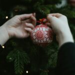 two hands holding a christmas ornament in front of a christmas tree