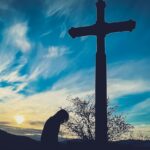 a person kneeling down in front of a cross