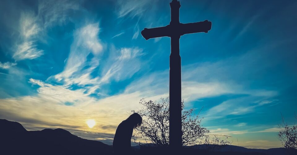 a person kneeling down in front of a cross