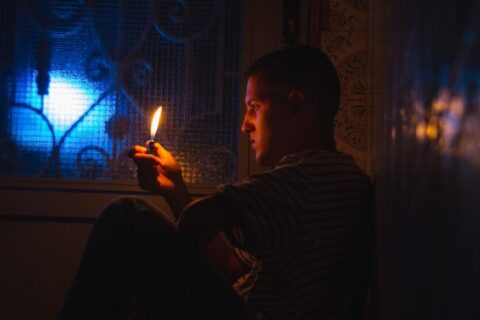 a man sitting in a dark room holding a lit candle