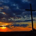 a cross sitting on top of a hill under a cloudy sky
