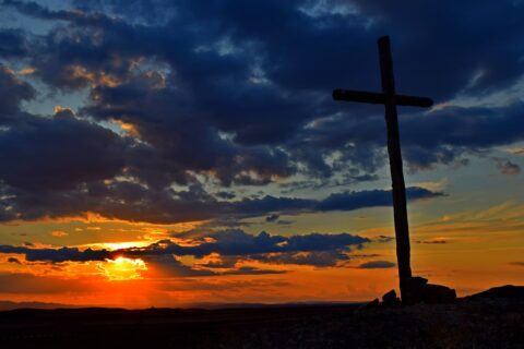 a cross sitting on top of a hill under a cloudy sky