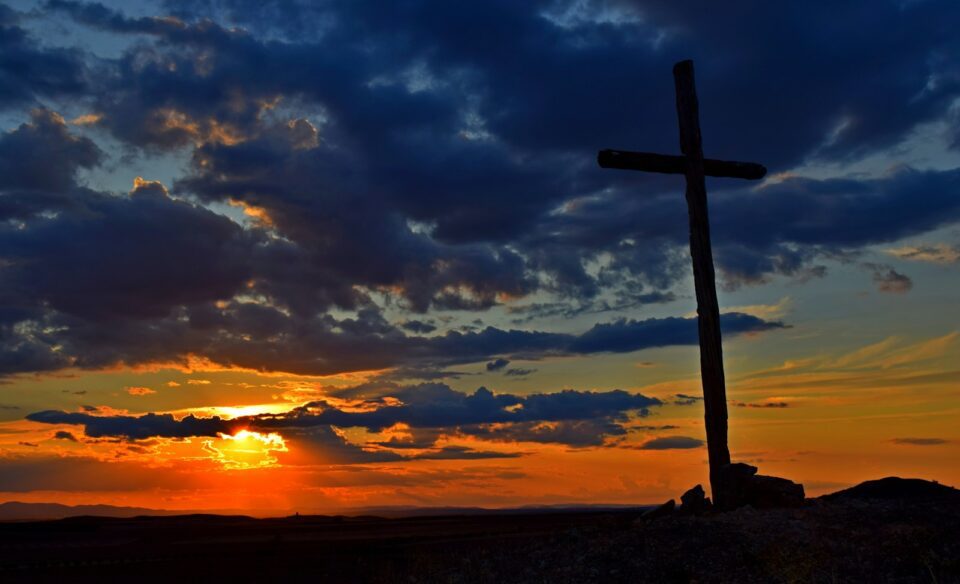 a cross sitting on top of a hill under a cloudy sky