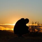 a silhouette of a person sitting on a hill at sunset