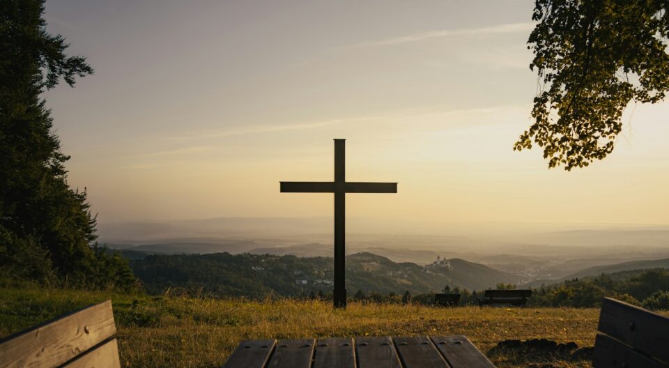 A cross stands on a hill overlooking the scenery.