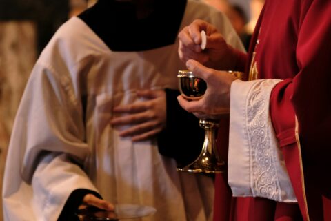 A priest is holding a glass of wine