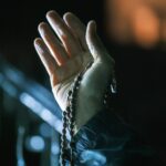 Hand holding rosary beads in dim light