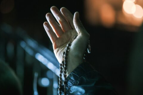 Hand holding rosary beads in dim light