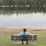 woman sitting on bench near lake during daytime