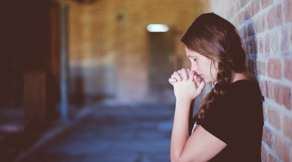 woman praying while leaning against brick wall