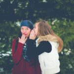 woman whispering on woman's ear while hands on lips