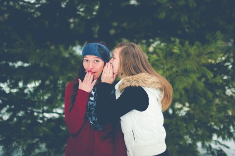 woman whispering on woman's ear while hands on lips