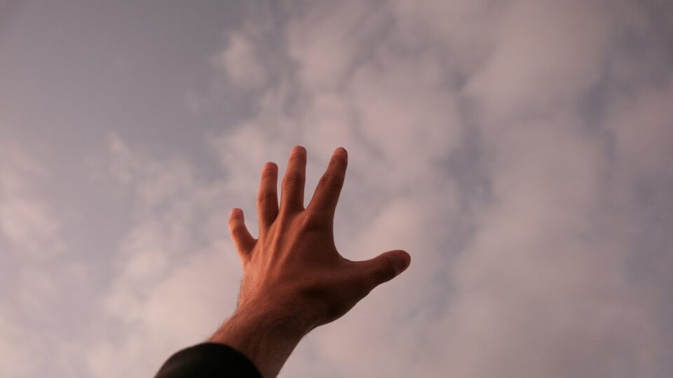 a person's hand reaching up into the sky