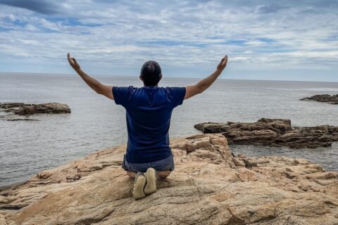 a man sitting on top of a rock near the ocean