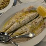 a white plate topped with fish next to a bowl of noodles