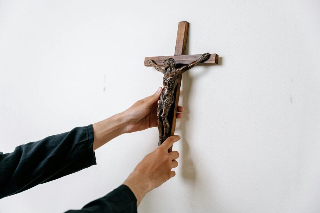 Close-up image of hands placing a wooden crucifix on a white wall emphasizing spirituality.