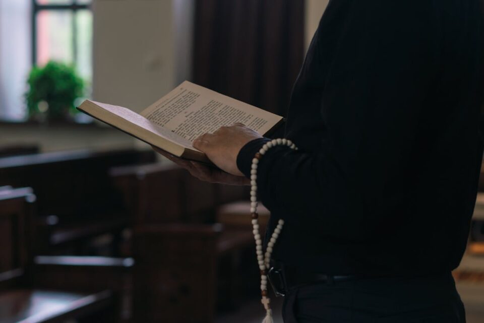 Person holding a holy book with prayer beads inside a church. Spiritual and religious setting.