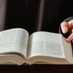 Close-up of a person turning pages of an open Bible on a wooden desk.