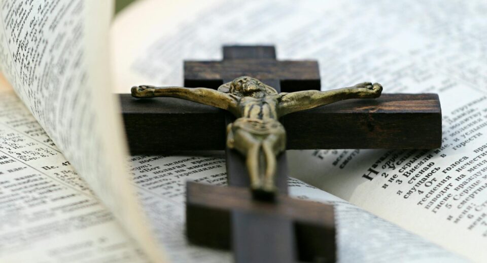 An open Bible with a brass crucifix on a dark wooden cross lying across it.