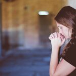 woman praying while leaning against brick wall