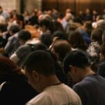 A crowd of people bowing their heads in prayer.