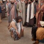 Isus prstom piše po zemlji dok okupljena gomila stoji u pozadini spremna na osudu