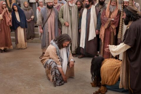 Isus prstom piše po zemlji dok okupljena gomila stoji u pozadini spremna na osudu