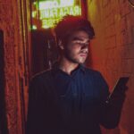 man in black dress shirt standing near red brick wall