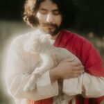 Man in robes holding a lamb in a field