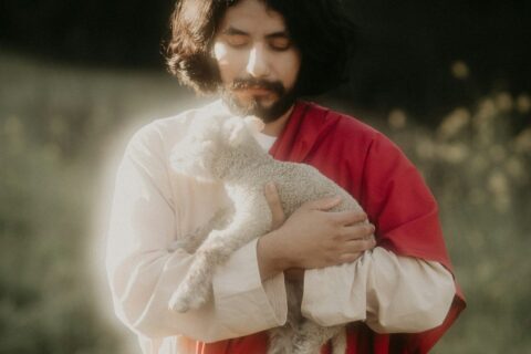 Man in robes holding a lamb in a field