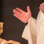 Svećenik tijekom svete mise moli raširenih ruku pokraj oltara na kojem se nalaze kalež, Biblija i liturgijske knjige.